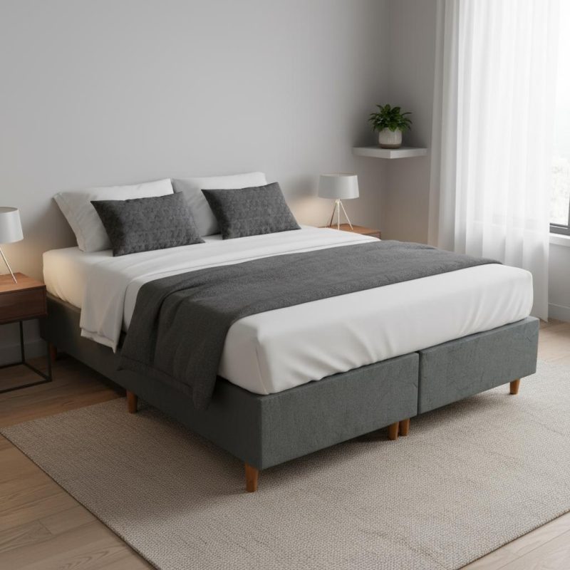 Base cama dividida tapizada en color gris oscuro con patas de madera en un dormitorio moderno.