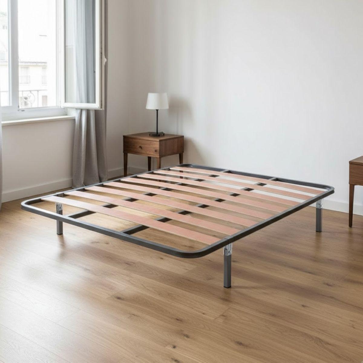 Somier de láminas de madera con bastidor y patas de metal gris sobre un suelo laminado de madera en una habitación iluminada.